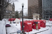 The Nova Scotia government has announced four sites that will host pallet shelters for the homeless with the first 19 shelters likely ready for occupancy sometime next month. Matthew Grant uses a broom to clean snow off ice fishing enclosures at a tent encampment in front of City Hall in downtown Halifax, Monday, Dec. 4, 2023. THE CANADIAN PRESS/Darren Calabrese