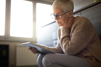 Serious senior woman using tablet computer indoors seems concerned