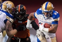 Winnipeg Blue Bombers' Andrew Harris (33) runs the ball as Patrick Neufeld, left, blocks B.C. Lions' Junior Luke during the first half of a CFL football game in Vancouver, on Saturday July 14, 2018. Running back Andrew Harris will sign a one-day contract with the Winnipeg Blue Bombers this month and retire as a member of the team, the CFL club said Friday. THE CANADIAN PRESS/Darryl Dyck