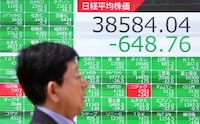 A man walks past an electronic board showing a share price of the Nikkei index of the Tokyo Stock Exchange in Tokyo on April 16.