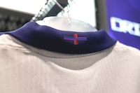 A view of Nike's designed St George's Cross on the back of the collar of the new England shirt, in London, Friday, March 22, 2024. England's new men's soccer team shirt is out and it's causing a bit of a stir. And it's not just the price that's vexing some. The decision by Nike to change the color of the St. George's Cross on the new shirt from the traditional red and white has even prompted the prime minister and the man who is favored to succeed him to make their displeasure known. (AP Photo/Kin Cheung)