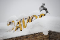 (FILES) In this file photo taken on January 22, 2018, an armed security personnel wearing camouflage clothing stands on the rooftop of a hotel, next to letters covered in snow reading "Davos", near the Congress Centre ahead of the opening of the 2018 World Economic Forum (WEF) annual summit.
