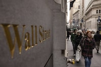 People walk past a Wall Street sign outside the New York Stock Exchange, Monday, Dec. 11.