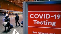 FILE - Travelers pass a sign near a COVID-19 testing site in Terminal E at Logan Airport, on Dec. 21, 2021, in Boston. The nation’s top public health agency is expanding a program that tests international travelers for COVID-19 and other infectious diseases. The Centers for Disease Control and Prevention currently operates a program at six U.S. airports that asks passengers from inbound international flights to agree to nose swabs and answer questions about their travel. (AP Photo/Charles Krupa, File)