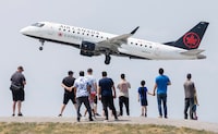 People watch an Air Canada plane take off at Trudeau Airport from Jacques de Lesseps Park in Montreal, Sunday, June 11, 2023.