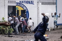 A Police officer throws a rock as opposition supporters run into a opposition leader Martin Fayulu's party house during a demonstration in Kinshasa on December 27, 2023. Police were deployed in the Democratic Republic of Congo's capital Kinshasa on December 27, 2023 during a banned demonstration against recent elections in the fragile central African state.Leading opposition politicians in impoverished but mineral-rich DRC have rejected last week's vote, which was marred by severe delays and bureaucratic disarray, and called for a demonstrations. (Photo by JOHN WESSELS / AFP) (Photo by JOHN WESSELS/AFP via Getty Images)
