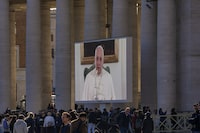 People watch Pope Francis on a giant monitor set up in St. Peter's Square at The Vatican, Sunday, Dec. 3, 2023, as he blesses the faithful gathered in the square for the traditional Angelus noon prayer. Francis skipped his weekly Sunday appearance at a window because suffering from a mild flu. (AP Photo/Andrew Medichini)