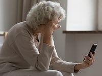 Sad elderly woman sit on sofa hold smartphone feels disappointed by received sms bad news, awful message, difficulties with modern device usage, unpleasant notification, stressed older person concept