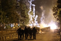 Riot police officers patrol as smoke billows from burnt vehicles on the third night of protests sparked by the fatal police shooting of a 17-year-old driver in the Paris suburb of Nanterre, France, Friday, June 30, 2023. The June 27 shooting of the teen, identified as Nahel, triggered urban violence and stirred up tensions between police and young people in housing projects and other neighborhoods. (AP Photo/Aurelien Morissard)