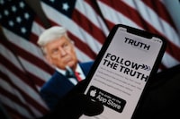 (FILES) In this illustration file photo taken on October 20, 2021, shows a person checking the app store on a smartphone for "Truth Social," with a photo of former US President Donald Trump on a computer screen in the background, in Los Angeles. - A new investment vehicle linked to f Trump's fledgling social media venture surged early October 22, 2021, before trading was temporarily halted due to the volatility. Shares of Digital World Acquisition Corp, which is set to merge with Trump's "TRUTH Social" media startup, surged more than 200 percent before being suspended for several minutes on the Nasdaq. (Photo by Chris DELMAS / AFP) (Photo by CHRIS DELMAS/AFP via Getty Images)