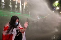 A woman reacts as law enforcement officers use a water cannon to disperse the crowd near the parliament building, during a rally to protest against a bill on "foreign agents" in Tbilisi, Georgia, May 1, 2024. Georgian parliament is set to debate the second reading of the bill described as authoritarian and Russian-inspired by Georgia's opposition and Western countries. REUTERS/Irakli Gedenidze