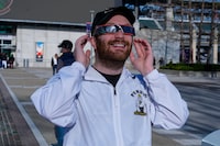 Craig Johnson, of West Lafayette,Ind., tries on his eclipse glasses at the Indianapolis Motor Speedway in Indianapolis, Monday, April 8, 2024. (AP Photo/Michael Conroy)
