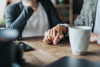 Close up of young Asian couple on a date in cafe, holding hands on coffee table. Two cups of coffee and smartphone on wooden table. Love and care concept