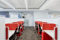Horizontal rows of separated red and white office cubicles with black desk chairs tucked in and red desk safes to the right side of each chair.