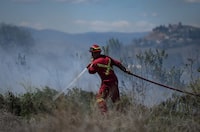 A firefighter directs water on a grass fire burning on an acreage behind a residential property in Kamloops, B.C., Monday, June 5, 2023. British Columbia's Peace River Regional District has cancelled an evacuation alert for areas around Chetwynd in the province's northeast. THE CANADIAN PRESS/Darryl Dyck