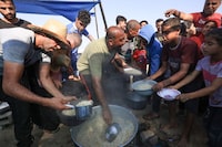 People distribute food to people at a makeshift camp for displaced people in Khan Yunis in the southern Gaza Strip on October 25, 2023, as battles between Israel and the Palestinian Hamas movement continue. (Photo by MAHMUD HAMS / AFP) (Photo by MAHMUD HAMS/AFP via Getty Images)