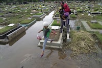 A family navigates the puddles at a flooded cemetery as they visit the grave of a relative ahead of the Muslim holy fasting month of Ramadan in Jakarta, Indonesia, Friday, March 8, 2024. Prior Ramadan, the holiest month in Islamic calendar, Indonesian Muslims followed local tradition to visit cemeteries to pray for their deceased loved ones. (AP Photo/Dita Alangkara)