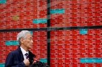 A man walks past an electronic board displaying stock prices of Nikkei 225 listed on the Tokyo Stock Exchange along a street in Tokyo on April 4.