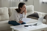 Stressed unhappy woman received bad news, unexpected debt or bankruptcy, sitting on couch alone, frustrated female holding paper letter, pondering problem solution, planning budget