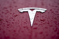 FILE - A Tesla logo has rain drops on it Feb. 27, 2024, in Charlotte, N.C. After reporting dismal first-quarter sales, Tesla is planning to lay off about a tenth of its workforce as it tries to cut costs, multiple media outlets reported Monday. (AP Photo/Chris Carlson)