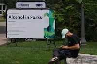 A report by city staff says a pilot project that allowed Torontonians to sip on beer, wine, spirits and other booze at select parks can safely become a fixture in the city should council vote in favour of doing so. A person sits near to a sign notifying the public of the start of a pilot project by the City Toronto to allow drinking alcohol in public parks, in Trinity Bellwoods Park, in Toronto, Wednesday, Aug. 2, 2023. THE CANADIAN PRESS/Chris Young