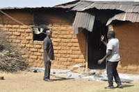 People stand in front of a burnt house following an attacked by gunmen in Bokkos, north central Nigeria, Tuesday, Dec. 26, 2023. Nigerian officials and survivors say at least 140 people were killed by gunmen who attacked remote villages in north-central Nigeria's Plateau state in the latest of such mass killings this year blamed on the West African nation's farmer-herder crisis. (AP Photo)