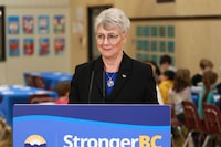 BC Finance Minister Katrine Conroy answers questions from reporters after serving up a hot lunch for students at Ruth King Elementary during a photo-op ahead of the budget while in Langford, B.C., on Feb. 27, 2023. An audited public accounting of British Columbia's financial records shows the province posted a budget surplus of $704 million in the 2022-2023 budget year. THE CANADIAN PRESS/Chad Hipolito