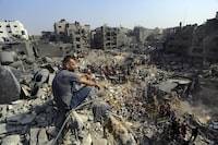 FILE - A man sits on the rubble as others wander among debris of buildings that were targeted by Israeli airstrikes in Jabaliya refugee camp, northern Gaza Strip, Wednesday, Nov. 1, 2023. A new U.N. report paints a stark picture of the devastating collapsing Palestinian economy after a month of war and Israel’s near total siege of Gaza. (AP Photo/Abed Khaled, File)