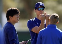 FILE - Los Angeles Dodgers' Shohei Ohtani, center, with interpreter Ippei Mizuhara, left, holds up his hands as he talks with a trainer during spring training baseball workouts in Phoenix, March 3, 2024. Mizhuhara has been fired by the Dodgers following allegations of illegal gambling and theft. (AP Photo/Carolyn Kaster,File)