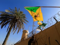 FILE PHOTO: A member of Hashd al-Shaabi (paramilitary forces) holds a flag of Kataib Hezbollah militia group during a protest to condemn air strikes on their bases, outside the main gate of the U.S. Embassy in Baghdad, Iraq December 31, 2019. REUTERS/Thaier al-Sudani