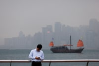 FILE PHOTO: A man checks his phone at the waterfront, with a tourist junk boat in the backdrop, on a foggy day in Hong Kong, China, March 6, 2024. REUTERS/Tyrone Siu/File Photo