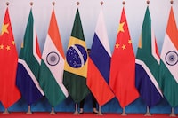 FILE PHOTO: A staff worker stands behind the national flags of Brazil, Russia, China, South Africa and India to tidy the flags before a group photo during the BRICS Summit at the Xiamen International Conference and Exhibition Center in Xiamen, southeastern China's Fujian Province, China September 4, 2017. REUTERS/Wu Hong/Pool