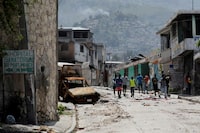 People walk past a damaged car in the Carrefour Feuilles neighborhood, which was deserted due to gang violence, in Port-au-Prince, Haiti March 19, 2024. REUTERS/Ralph Tedy Erol     TPX IMAGES OF THE DAY