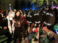 Pro-Palestine protesters with arms linked move out of the way as police move to clear a protest encampment at the University of Calgary campus, in Calgary, Alta., Thursday, May 9, 2024. The university said protesters at the encampment were trespassing and asked for help from police, who arrived in riot gear and issued multiple warnings for the crowd to disperse before starting to tear down fencing and tents. THE CANADIAN PRESS/Noah Korver