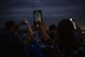 Canada's two largest mobile carriers say bolstered capacity helped their networks handle the extra wireless traffic in hot spot regions where tens of thousands gathered to take in Monday's total solar eclipse. People use their phones to document the total solar eclipse in Niagara Falls, Ont., on Monday, April 8, 2024. THE CANADIAN PRESS/Aaron Lynett