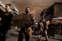 An Israeli soldier carries a box of sandwiches as he walks with a fellow soldier through the Machane Yehuda market under a sky darkened by nearby wildfires, in Jerusalem, Sunday, Aug. 15, 2021.(AP Photo/Maya Alleruzzo)