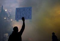 A person holds a 'Black Lives Matter' sign as a heavy cloud of tear gas and smoke rises after being deployed by Seattle police as protesters rally against police brutality and the death of George Floyd, in Seattle, Washington, on June 1, 2020.