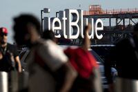 FILE - Travelers make their way near a JetBlue sign ahead of the Fourth of July holiday weekend at John F. Kennedy International Airport on June 28, 2022. in New York. Emergency responders evacuated a JetBlue flight at JFK International Airport in New York City as a result of a laptop emitting smoke on a plane Saturday evening, Dec. 24, officials said. (AP Photo/Julia Nikhinson, File)