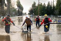 San Diego firefighters help Humberto Maciel rescue his dog  from his flooded home in Merced, California, on January 10, 2023. - Relentless storms were ravaging California again Tuesday, the latest bout of extreme weather that has left 14 people dead. Fierce storms caused flash flooding, closed key highways, toppled trees and swept away drivers and passengers -- reportedly including a five-year-old-boy who remains missing in central California. (Photo by JOSH EDELSON / AFP) (Photo by JOSH EDELSON/AFP via Getty Images)