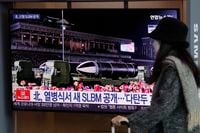 A woman walks past a TV screen showing a news program reporting about North Korea's military parade, at the Seoul Railway Station, in Seoul, South Korea, on Jan. 15, 2021.
