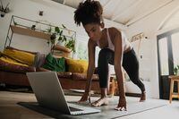 Beautiful young mixed race female exercising at home, online workout on laptop